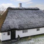 Wohnhaus mit strohgedecktem Dach und weißer Fassade. Nummer 61. Schnee bedeckt den Boden und das Dach.