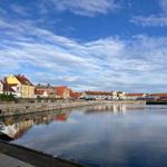 Hafen mit Segelyacht und Reflexionen von Häusern im Wasser.