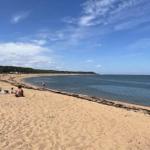 Strand mit Sand, Meer und einigen Menschen in der Ferne.