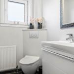 Badezimmer mit Toilette, Waschbecken und Spiegel. Fenster mit Blumen auf Sims.