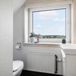 Badezimmer mit Fenster, Waschbecken und Toilette. Draußen sind Häuser und Bäume sichtbar.