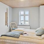 Schlafzimmer mit Bett, Stuhl und Fenster. Holzdecke und Kleidung auf dem Bett.