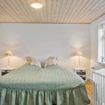 Schlafzimmer mit Bett, Nachttischen und Babybett. Holzdecke und Fenster sichtbar.