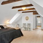 Schlafzimmer mit Dachschrägen, Holzbalken und hellem Holzboden.