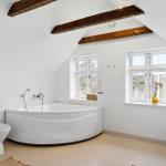 Badezimmer mit Badewanne, Fenstern und Holzbalken an der Decke.