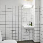 Badezimmer mit Toilette, Waschbecken und Spiegel an weißen Fliesenwänden.