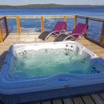 Whirlpool auf Terrasse mit Blick auf See und zwei Liegestühle mit lila Decken.