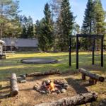 Fire pit, trampoline, and playground in the garden with log bench and trees.