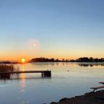 Sonnenuntergang über ruhigem See mit Steg und Picknicktisch