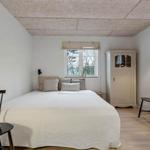 Schlafzimmer mit Bett, Schrank und zwei Stühlen. Fenster mit Blick auf Bäume.