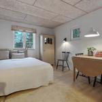 Schlafzimmer mit Bett, Tisch, Stühlen und Fenstern. Decke aus Holzplatten.