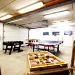 Garagenraum mit Tischtennisplatte, Backgammon und Fussballtisch. Holzstühle und Deckenleuchten sichtbar.