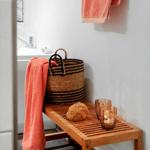 Holzbank mit Seifenschaum, Glas und Korb in Bad. Handtuch an Wand hängend.