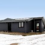 Moderne, schwarz getäfelte Ferienhaus mit Dachgauben und schneebedecktem Grundstück.