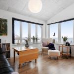 Wohnzimmer mit großem Fensterblick aufs Meer, Sofa, Sessel und Holzmöbel.