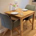 Holztisch mit zwei Stühlen, Tischdecke, Gläser und Blumen in Vase.