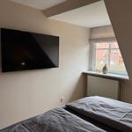 Schlafzimmer mit Bett, Wandfernseher und Fenster mit Blick nach draußen.