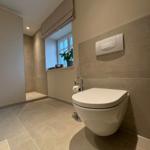 Badezimmer mit Toilette, Fenster und Fliesenboden.