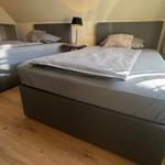 Zwei Betten mit grauer Bettwäsche und Kopfteil in einem Schlafzimmer mit Holzboden und Dachschrägen.