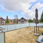 Terrasse mit Tisch, Stühlen und Sonnenschirm. Blick auf Häuser und Bäume.