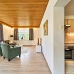 Wohnzimmer mit grünen Sesseln und Küche mit Holzschränken