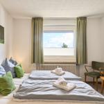 Zimmer mit Doppelbett, Fenster, Stuhl und Wandbild