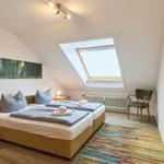 Schlafzimmer mit Dachschrägen, Bett, Fenster und Stuhl.