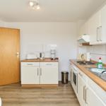 Küche mit Arbeitsplatte, Spüle und Kochfeld. Tür führt in Wohnbereich.