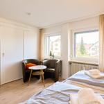 Zwei Betten, zwei Fenster, zwei Sessel und ein kleiner Tisch.