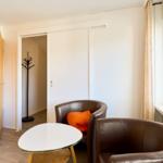 Zwei braune Sessel und ein runder Tisch stehen vor einem Fenster mit grünen Dekorationen.