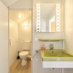 Badezimmer mit Waschbecken, Spiegel und Toilette im Hintergrund.