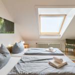 Zimmer mit Dachschrägen, Dachfenster, Bett und Stuhl.