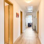 Flur mit Holzboden, Türen und Wandbildern. Durchgang zum Wohnbereich mit Sitzgelegenheit.