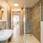 Badezimmer mit Dusche, Waschbecken und Spiegel. Durchgang zur Schlafzimmer.