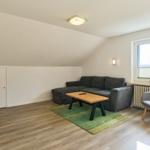 Wohnzimmer mit Sofa, Sessel und Fernseher. Holzboden und Fenster mit Blick.