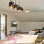 Wohn- und Essbereich mit TV, Sofa und Esstisch. Dachgeschoss mit Holzboden und Lampen.