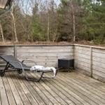Terrasse mit Liegestuhl und Tisch, umgeben von Holzwänden und Wald.