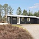 Schwarzes Haus mit weißer Tür und Fensterrahmen, umgeben von Bäumen und Heide.