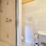 Badezimmer mit Dusche, Waschbecken und Toilette. Weiße Fliesen und Holzdecke.