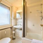 Badezimmer mit Dusche, Waschbecken und Toilette. Fenster mit getöntem Glas.