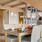 Esszimmer mit Holzwand und Esstisch mit Stühlen. Küche im Hintergrund.
