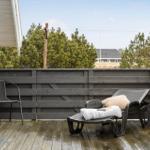 Terrasse mit Liegestuhl und Stuhl, umgeben von dunklem Holzgeländer und Bäumen.