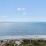 Weitläufiger Strand mit sanften Wellen unter klarem Himmel.