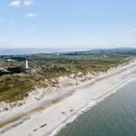 Aerofoto einer Küstenlandschaft mit Strand, Dünen und Leuchtturm.