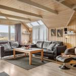 Wohnzimmer mit Ledersofa, Sessel und Holztisch. Holzwände und Dachbalken. Fenster mit Blick nach draußen.