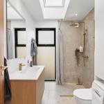 Badezimmer mit Dusche, Waschbecken und Toilette unter Dachfenster.