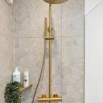 Duschkopf mit goldfarbener Armatur an Marmorwand