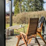 Terrasse mit Holzstuhl, Tisch und Decke. Hintergrund: Gras, Sträucher und Bäume.