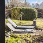 Zwei Liegestühle stehen im Garten vor einem Heckenzaun.
