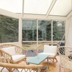 Terrace with rattan furniture and hanging chair. Glass walls and wooden floor.